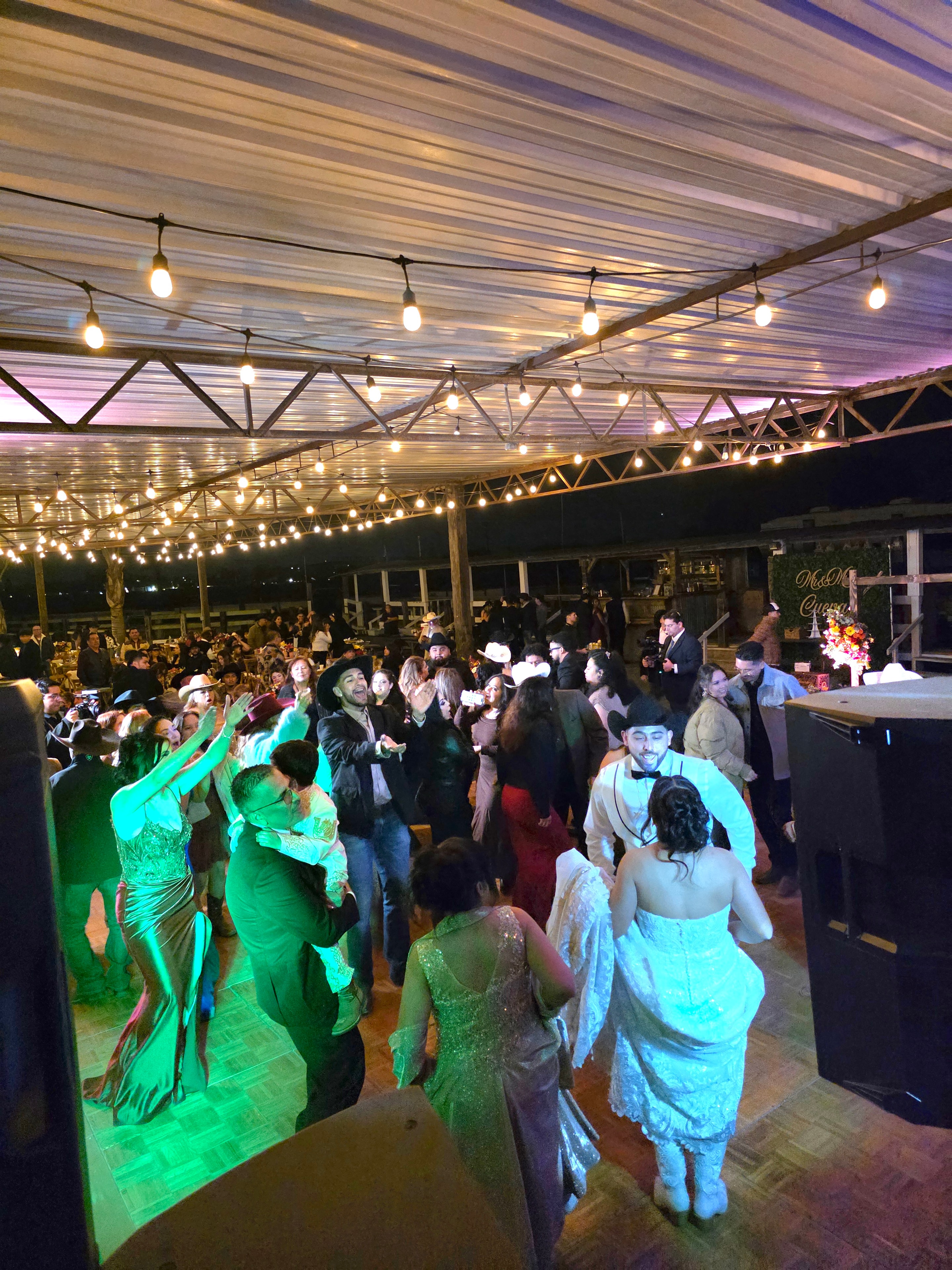 Packed wedding dance floor with string lights and green uplighting at DJ event