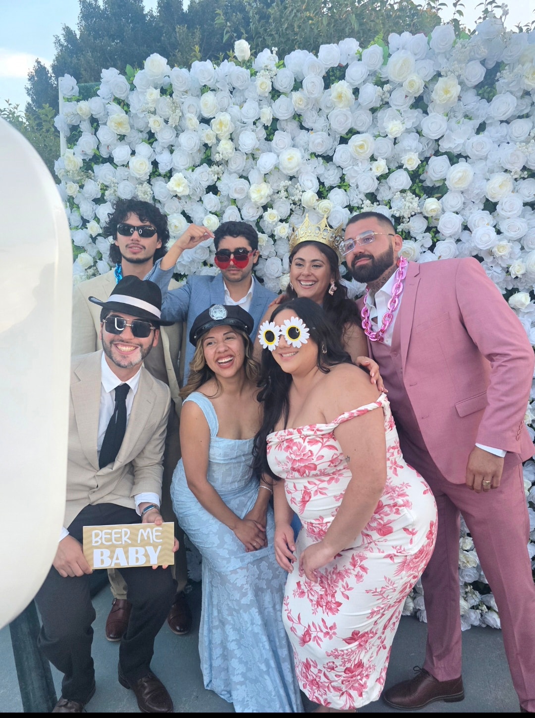 Wedding guests posing with fun props in front of white flower wall